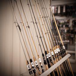 Selection of fishing rods by length and action rating leaning against a softly lit wall in a tackle store